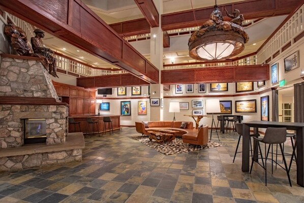 A spacious lobby with a stone fireplace, wooden ceiling beams, a large chandelier, and a seating area with a coffee table.