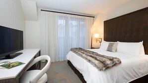 A hotel room with a bed, a desk with a computer, a chair, a TV, and a window with curtains. - Charlie's Slopeside: Best Location BC Village! Creekside Unit, Walk to Lifts, Ski School, Dining (Beaver Creek)