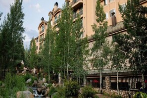 A multi-story hotel with balconies, surrounded by trees and a small waterfall. - Charlie Rentz: Best Location BC Village! Creekside Unit, Walk to Lifts, Ski School, Dining (Beaver Creek)