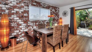 A dining area with a brick wall, wooden table, wicker chairs, and two floor lamps.