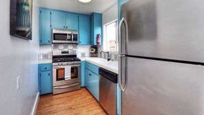 A compact kitchen with blue cabinets, a stainless steel refrigerator, a microwave, a stove, and a dishwasher.