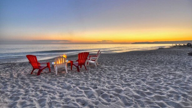 A beach with red chairs and a table, suggesting a dining area.
