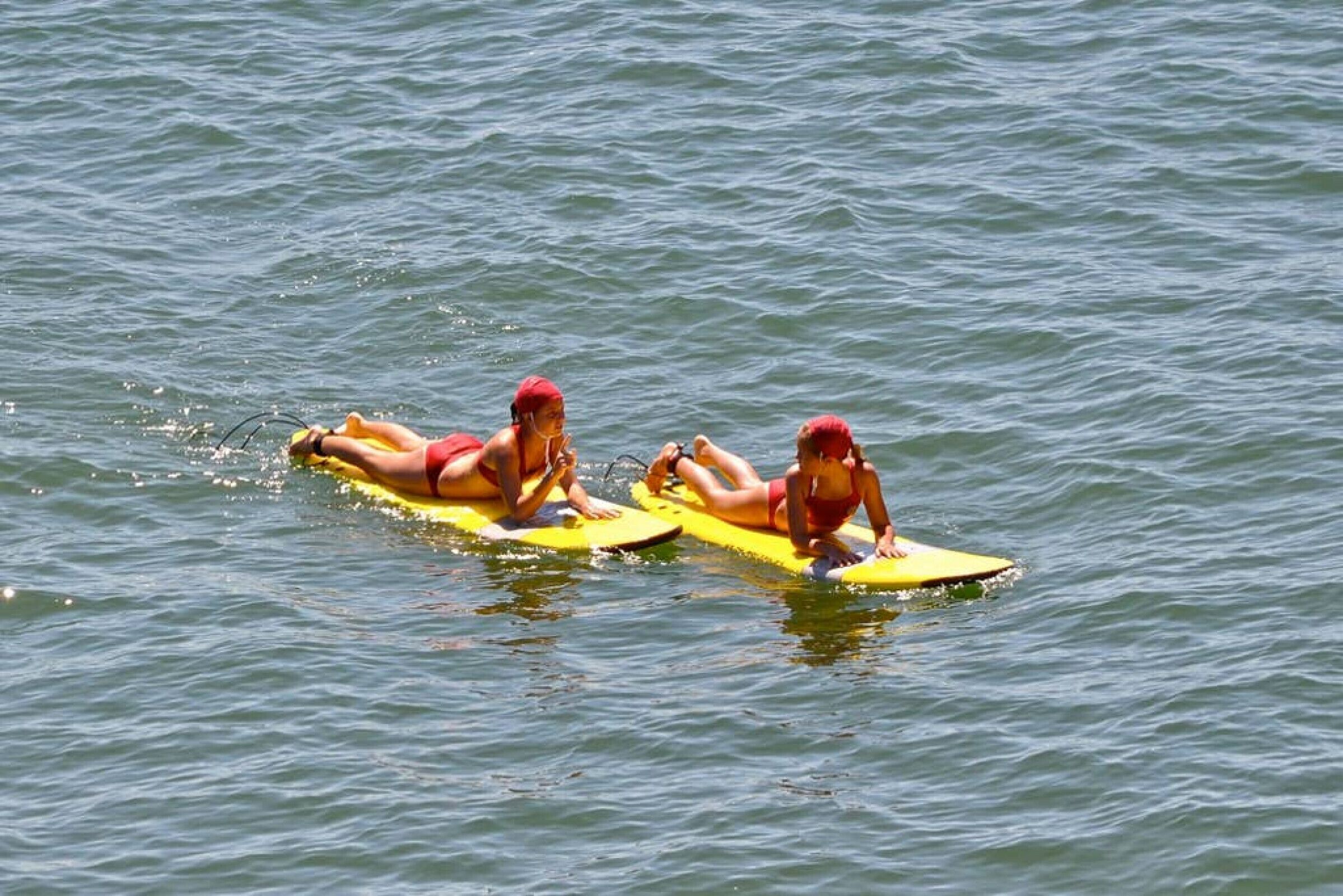 Duas pessoas deitadas em pranchas de surf na água.