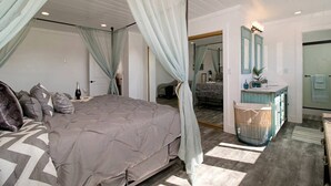 Un dormitorio con una cama grande, un tocador con espejo y una ventana con cortinas.