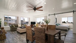 Amplia sala de estar con techo de madera, una mesa de comedor con sillas de mimbre, un sofá y una cama con vistas.
