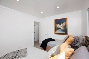 Une chambre à coucher avec un lit, des oreillers, un tableau et une porte donnant sur une autre pièce.