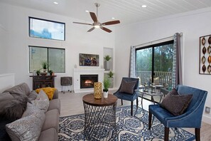 Un salon moderne doté d’une cheminée, d’un ventilateur de plafond et de grandes fenêtres.