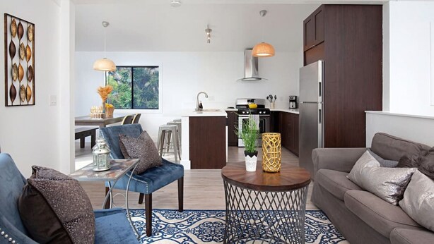 A modern living room with a sofa, a coffee table, and a dining area with a table and chairs. There is a kitchen area with a stove, refrigerator, and cabinets. - Fabulous Townhouse, close to beach, town and harbor (Dana Point)