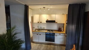 Eine kompakte Küche mit weißen Schränken, einer Edelstahl-Spüle und einem eingebauten Backofen.