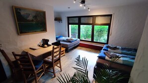 Ein kleines Zimmer mit einem Bett, einem Schreibtisch und einem Stuhl. Es gibt ein Fenster mit Jalousien, einen Heizkörper darunter und ein Bild an der Wand.