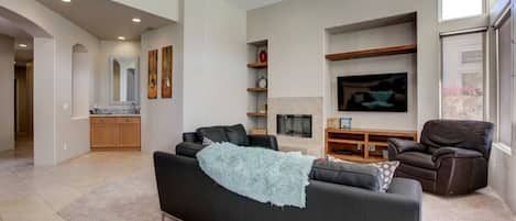 Una sala de estar moderna con un sofá negro, un televisor y una chimenea.