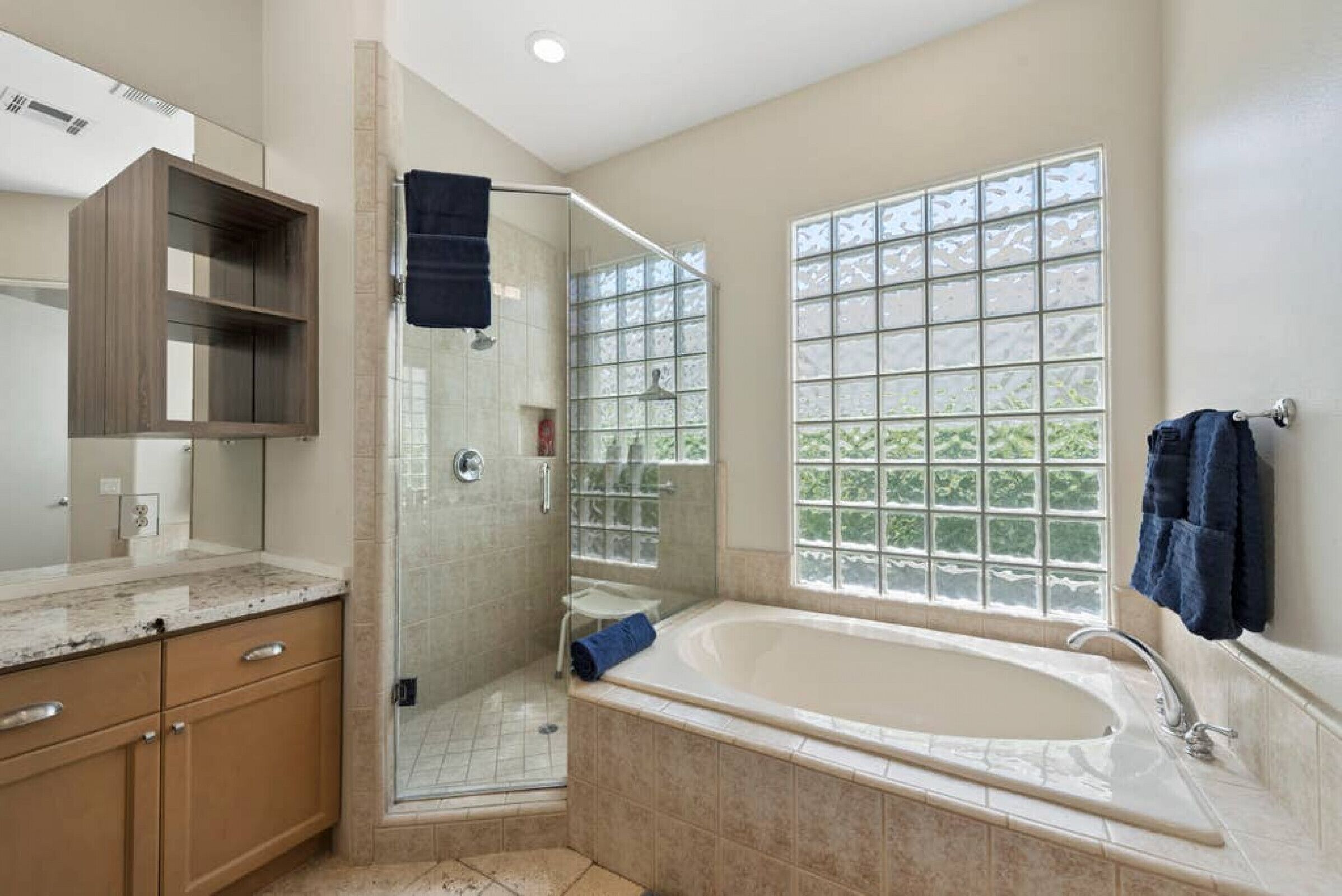 A bathroom with a walk-in shower, a large bathtub, a glass shower enclosure, and a window with a view.