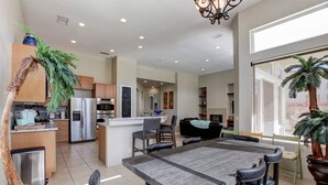 A modern kitchen with a central island, stainless steel appliances, and a dining area with a wooden table and chairs. - Waterslide, heated pool home, PGA West 6th tee box (La Quinta)