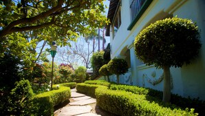 A stone pathway flanked by neatly trimmed hedges and a white building with a green trim and a small tree in front. - Garden Cottage Casita (San Clemente)