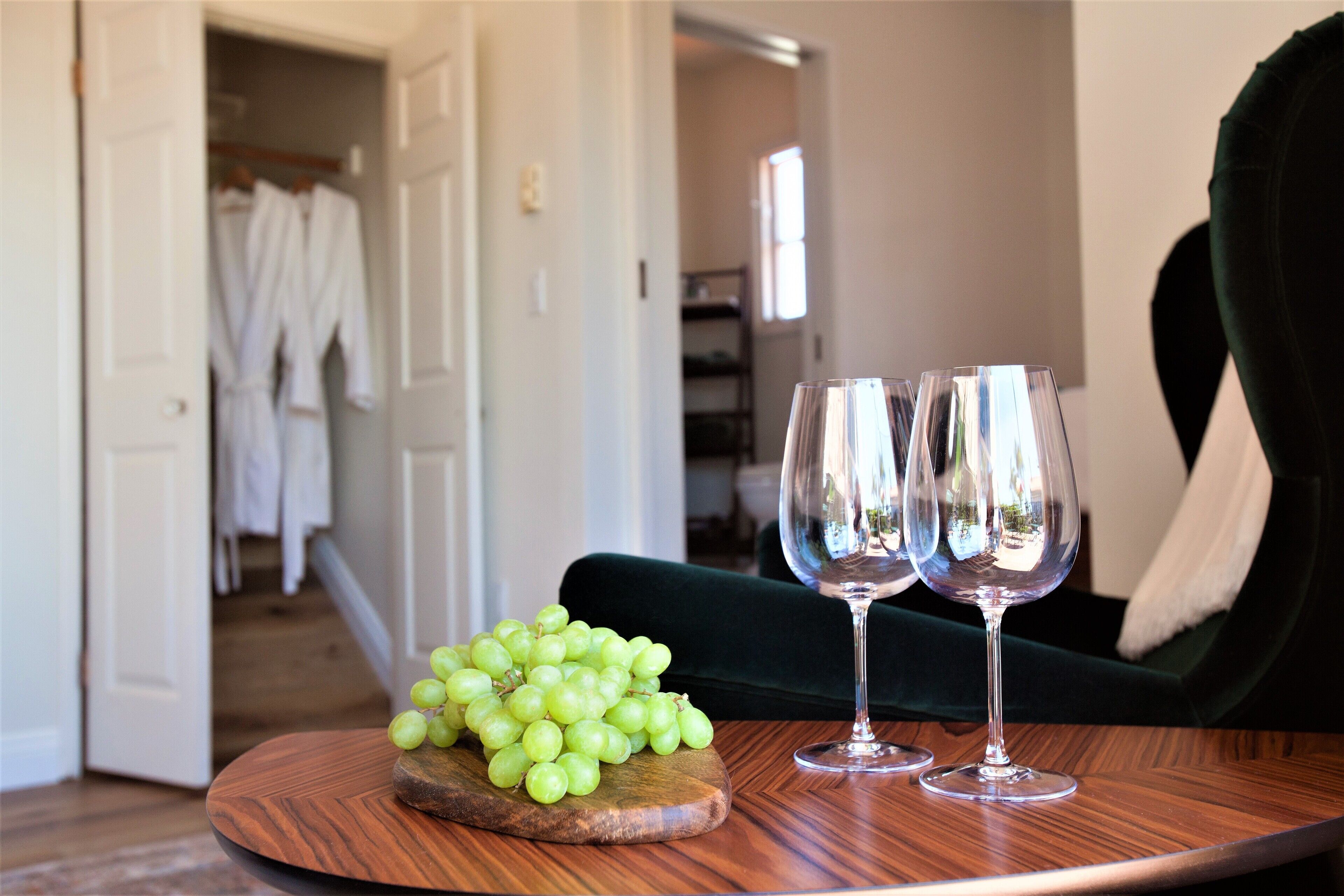 A wooden table with a wooden board holding green grapes and two wine glasses.