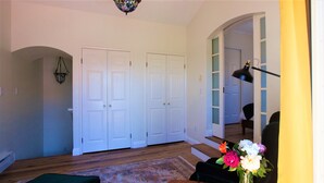 A living room with a wooden floor, a green sofa, a small table with a vase of flowers, and a staircase leading to another room. - Garden Cottage Casita (San Clemente)