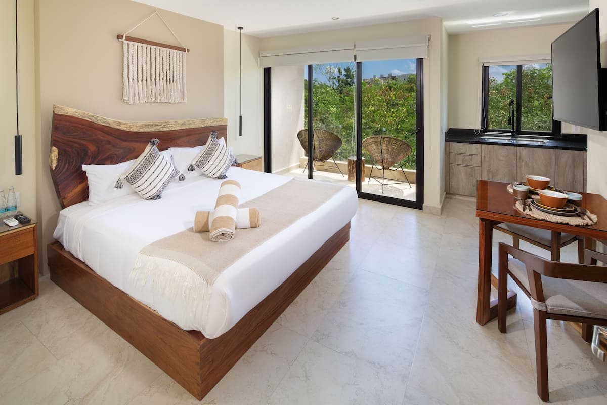 A modern hotel room with a large bed, a dining area, and a TV.
