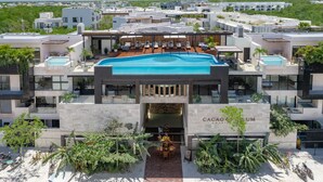 Ein modernes Hotel mit Pool auf dem Dach, mehreren Balkonen und üppiger Bepflanzung.