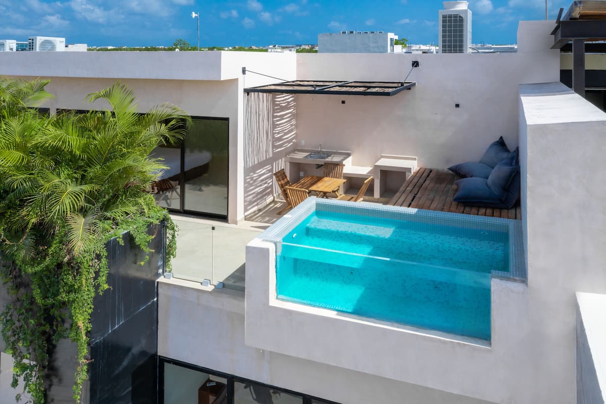 A rooftop pool area with a wooden deck, seating, and a view of the city skyline.