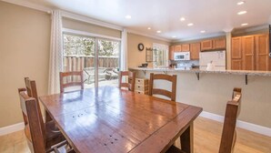 Un comedor con una mesa y sillas de madera, una cocina con armarios de madera, y un gran ventanal corredizo que da a un patio exterior.