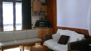 Una sala de estar con un sofá, una silla de mimbre, una mesita y un aparador con libros.