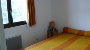 Un dormitorio con cama, ventana con cortinas, mesita de noche con lámpara y radiador.