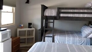 Un dormitorio con literas, un microondas, una mesita y una ventana.