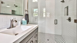 Un baño moderno con un lavamanos blanco, cabina de ducha con mampara de vidrio y suelo estampado.