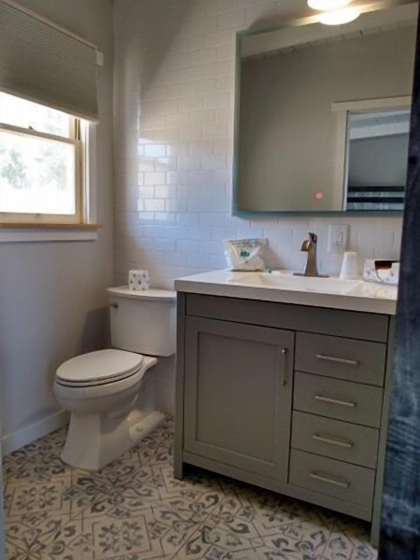 A bathroom with a toilet, a sink with a mirror, and patterned floor tiles.