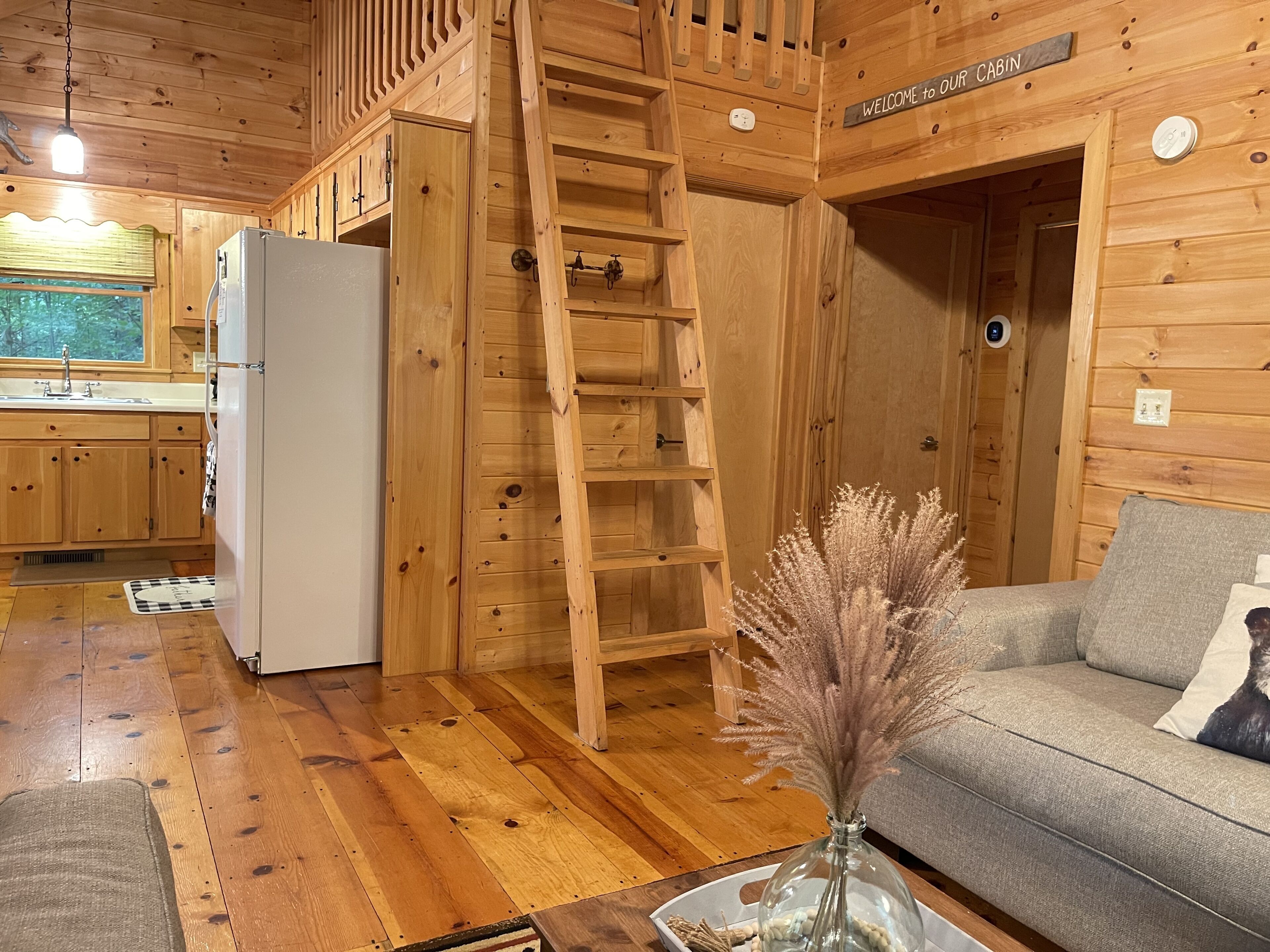 Een vakantiehuisje met houten details, een bank, een salontafel, een koelkast, een keukenhoek en een houten trap.