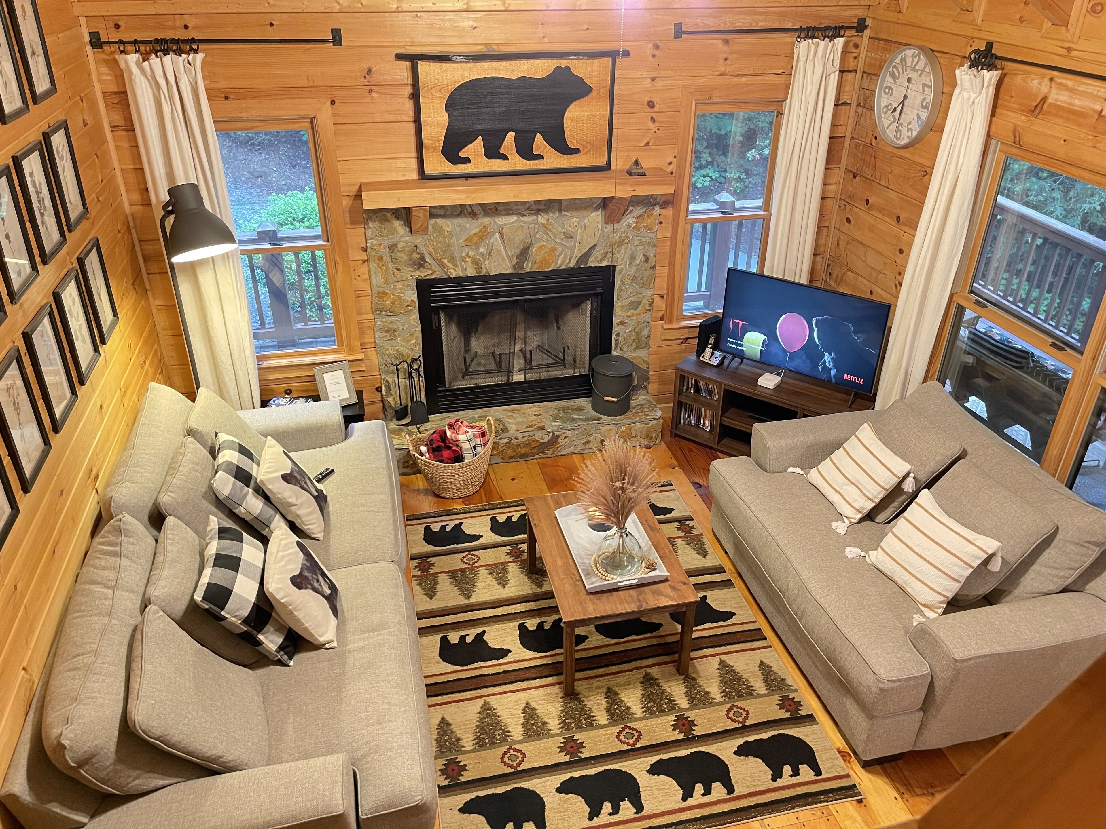 A cozy cabin-style living room with two sofas, a fireplace, a television, and framed pictures on the walls.