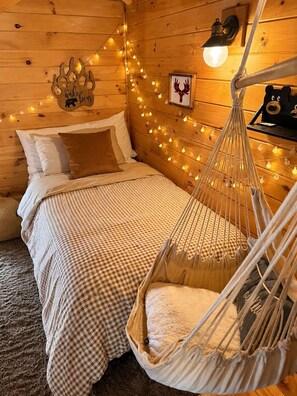 A cozy room with a bed, a hammock, string lights, and a wall-mounted lamp.