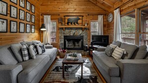 A cozy log cabin interior with two grey sofas, a fireplace, framed botanical prints, and a bear silhouette decoration. - Welcome to Bearadise! Charming cabin 10 minutes to downtown Blue Ridge! (Cherry Log)