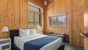 Un dormitorio con paneles de madera, una cama, mesitas de noche y una ventana con vista a las montañas.