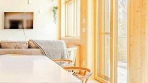Un interior moderno de madera con una mesa de comedor, sillas, un sofá y ventanas grandes.