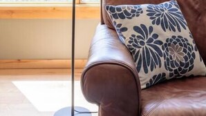 Ein Zimmer mit einem braunen Ledersofa, einer Stehlampe und einem Fenster mit Blick auf die Berge.