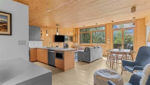A modern cabin interior with a wooden interior, a kitchen with a central island, a dining area, and a living room with a sofa and chairs. - Dolomites #203 - LEED Gold Certified! (Canmore)