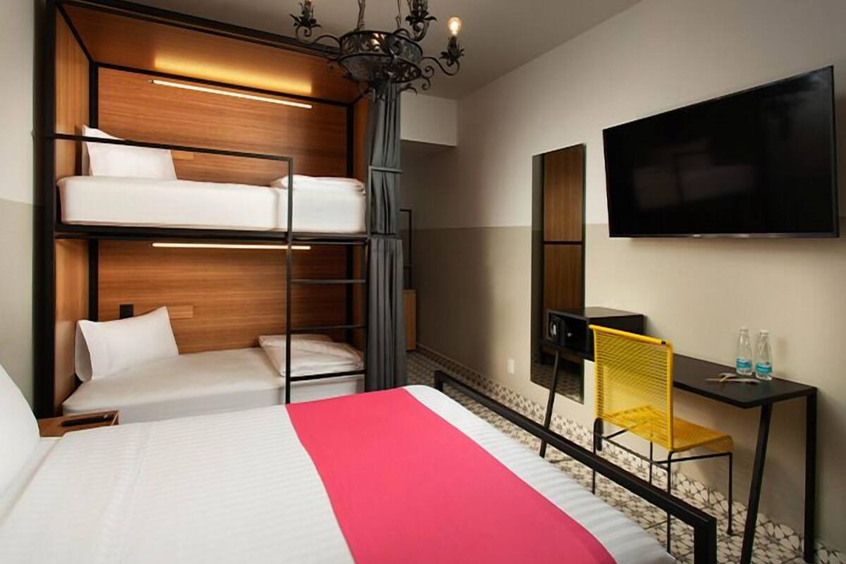 Een hotelkamer met stapelbedden, een bureau, een stoel, een televisie en een kroonluchter.