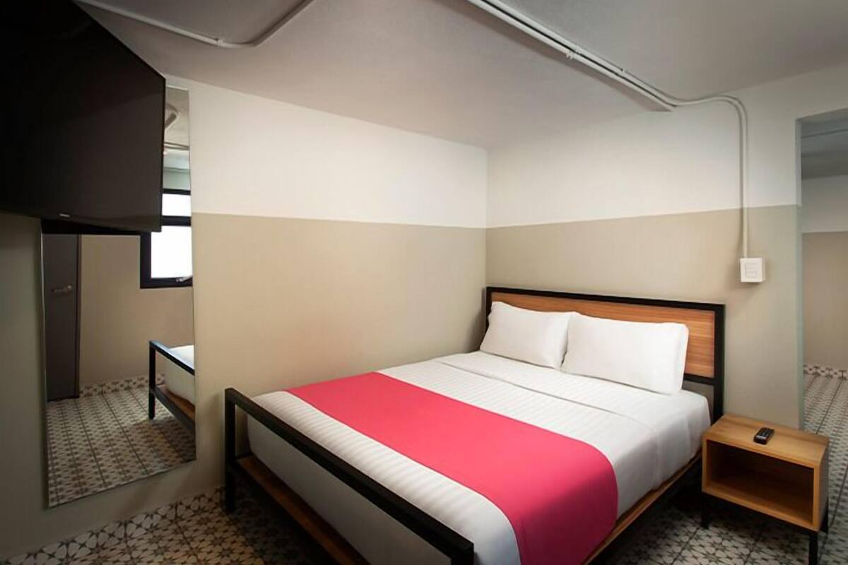 Een slaapkamer met een bed, nachtkastje, spiegel en een lamp.