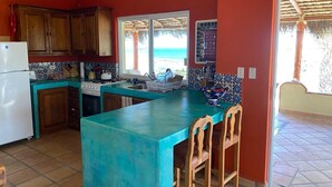 Una cocina con armarios de madera, un refrigerador blanco, una encimera turquesa y una ventana con vistas a la playa.
