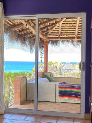 A room with a sliding glass door leading to a balcony with a view of the ocean.
