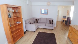 Un salon avec un canapé d’angle, une bibliothèque en bois et un tapis foncé.