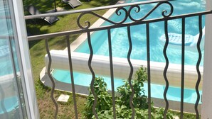 Une piscine bordée d’un muret en pierre et une zone herbeuse avec des chaises longues et des parasols.