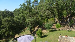 Un espace extérieur verdoyant, avec un mur de pierre, un parasol blanc et plusieurs chaises longues.