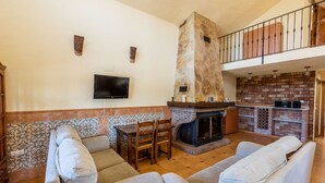 Un salon doté d’une cheminée en pierre, d’un téléviseur fixé au mur et d’un balcon avec une balustrade en bois.