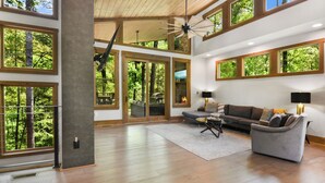 Ein großzügiger Wohnraum mit großen Fenstern, einer Holzbalkendecke und einem modernen Sofa.