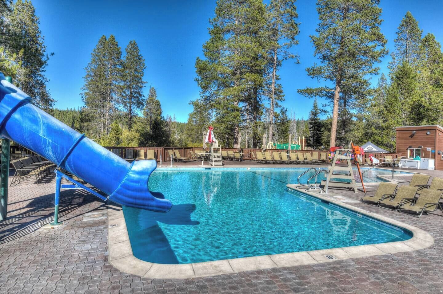 Une piscine avec un toboggan bleu, entourée de chaises longues et d’une terrasse en bois.