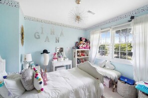 A bedroom with a bed, a dresser, a vanity, and a window with curtains.