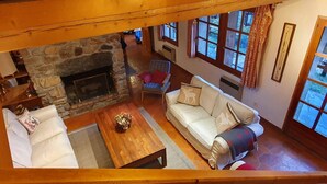 A cozy living room with a stone fireplace, a white sofa, a wooden coffee table, and a window with curtains.