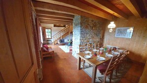 A dining area with a stone wall, wooden ceiling beams, and a staircase leading to a loft.